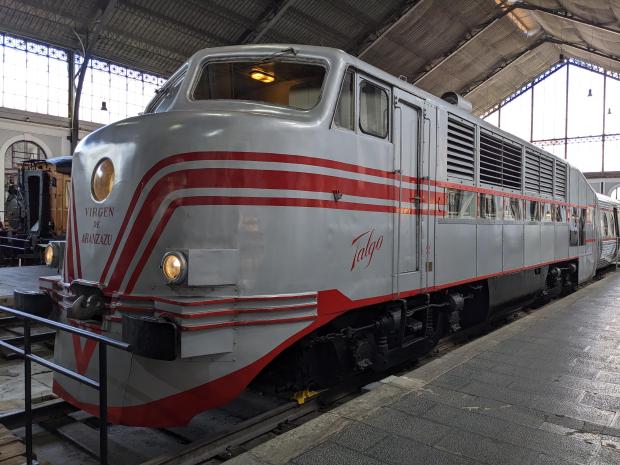 Picture of the control and power car of the Talgo II, named Virgen de Aránzazu. Painted gray with red strips and window cut outs to view the diesel-electric engine.