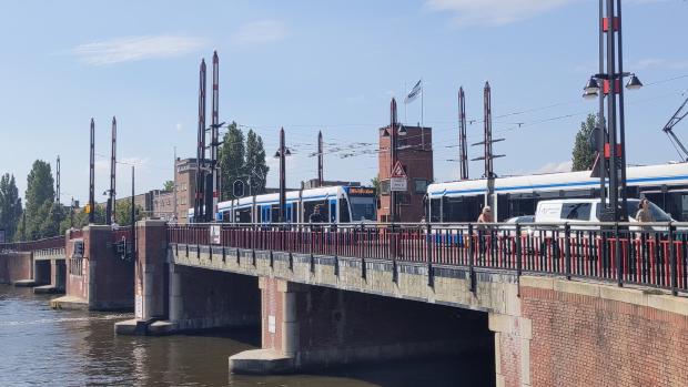 Berlagebrug on a sunny day with two trams crossing in opposite directions along with vehicles, pedestrians and cyclists.