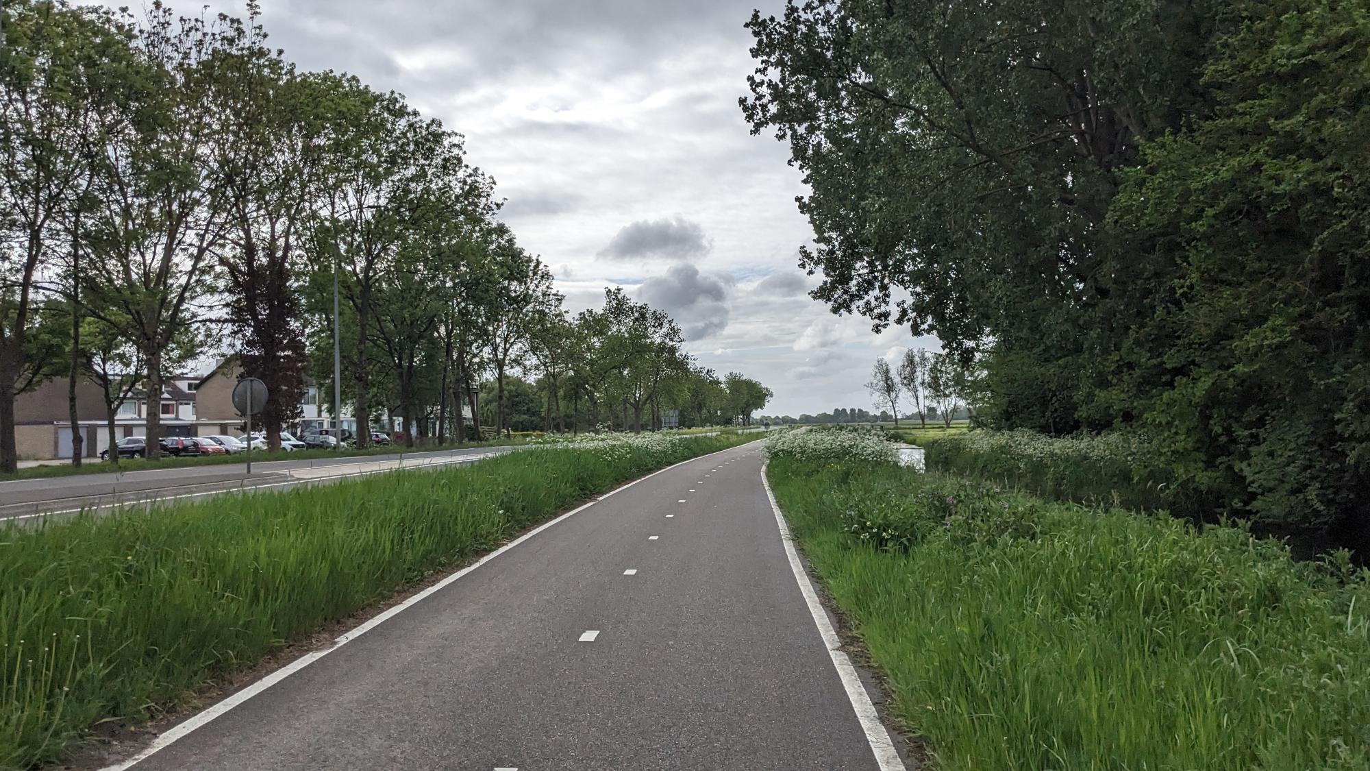 Seperate cycling path with green fields and trees to ther right a road to the left.
